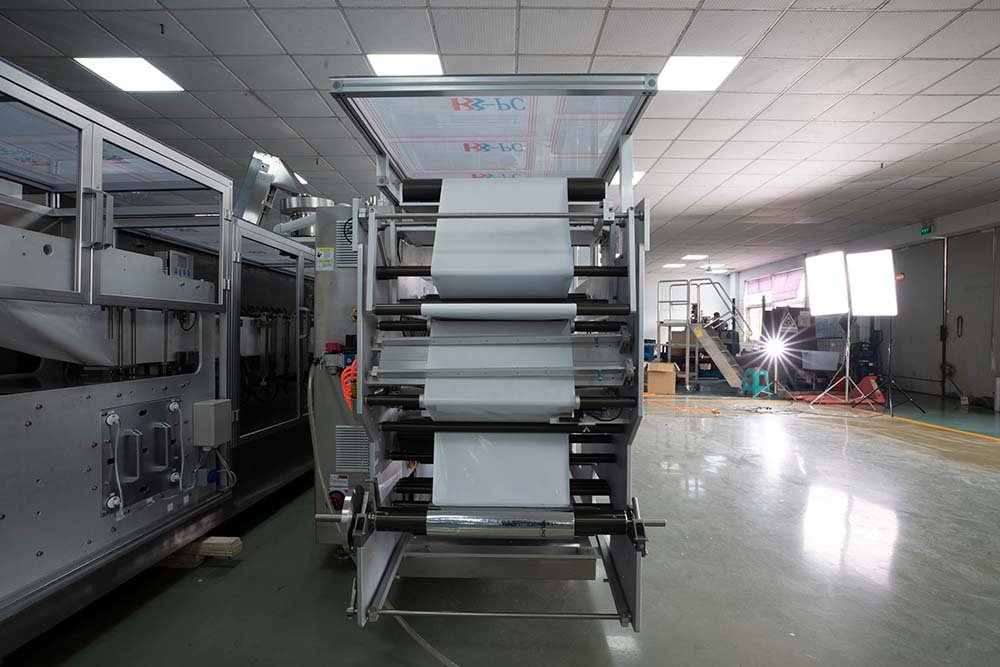 Rear view of HMS160 horizontal packaging machine showing multi-roller film unwind system