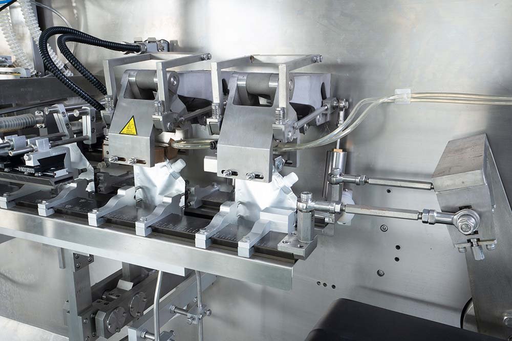 Dual filling nozzles and thermal top-sealing jaws working on spouted stand-up pouches inside an HFFS machine.